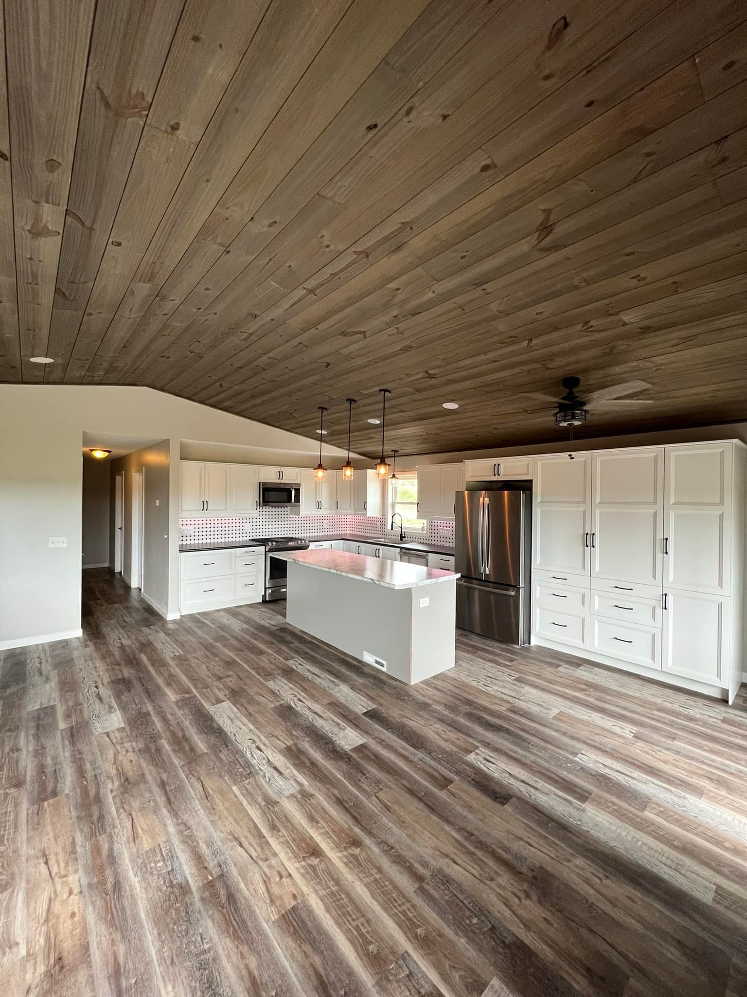 Finished open-plan kitchen with wood ceiling, white cabinets, and island